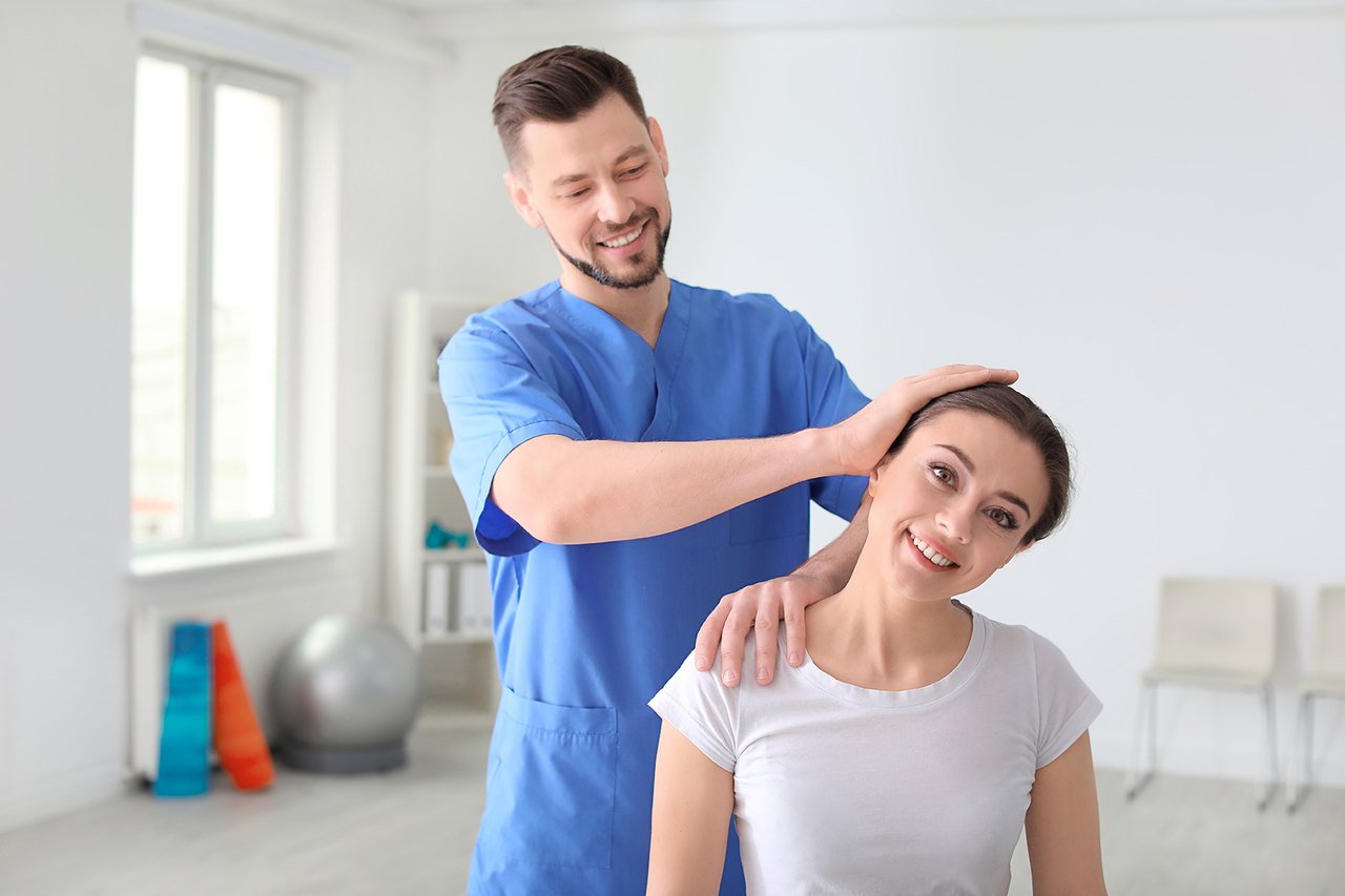 Male chiropractor gently adjusts a female patient's neck in a clinic.