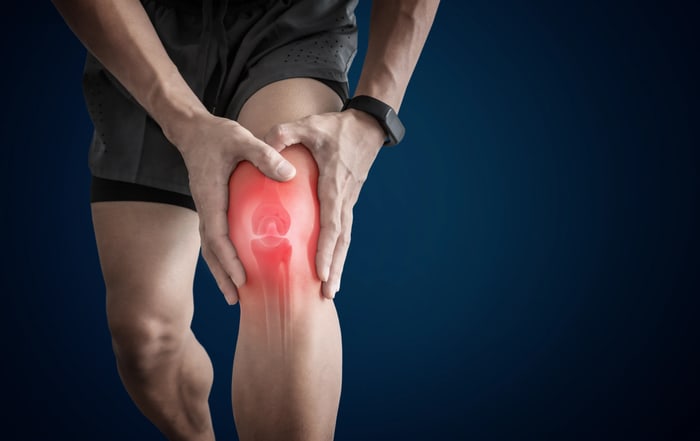 Man clutching his throbbing knee with both hands, indicating knee pain.